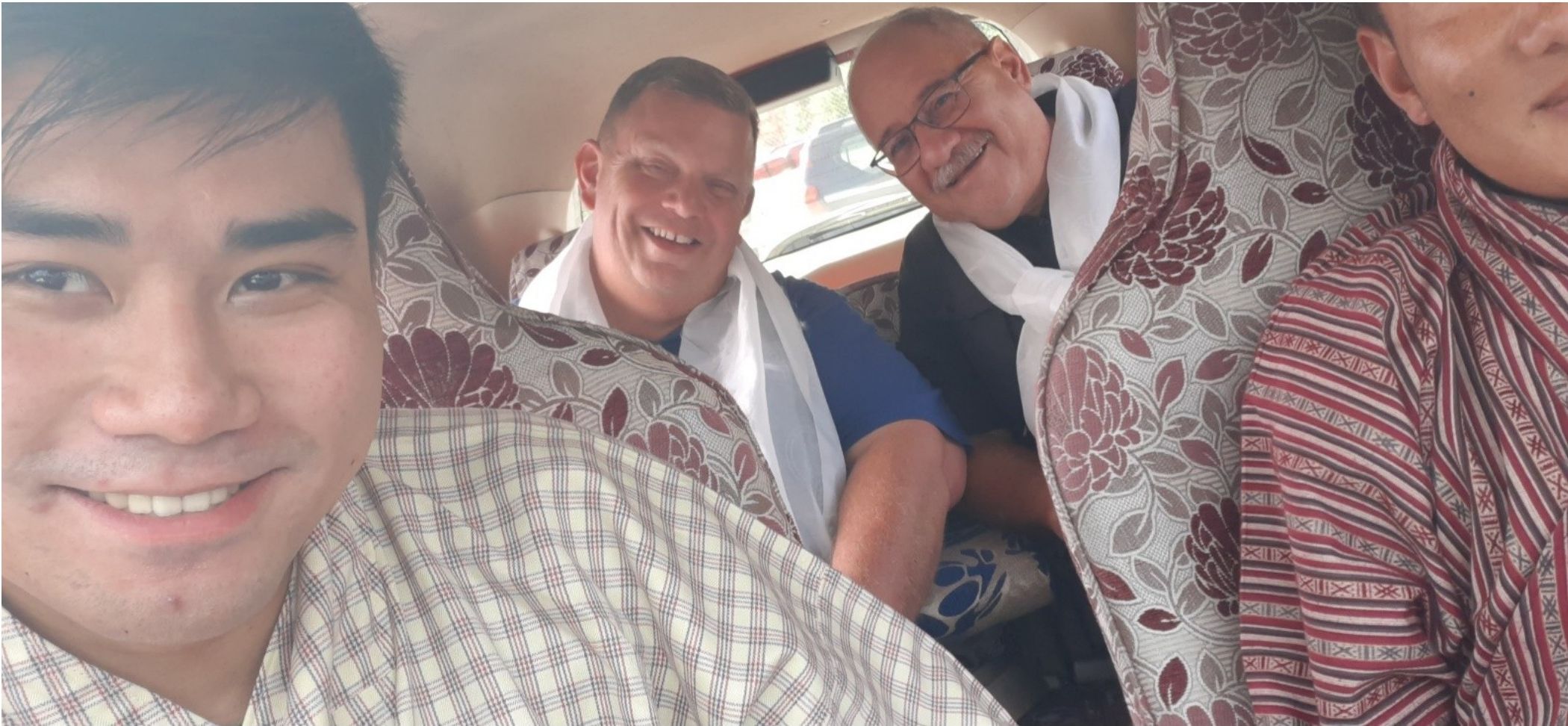 Guests in traditional Bhutanese attire smiling inside a vehicle